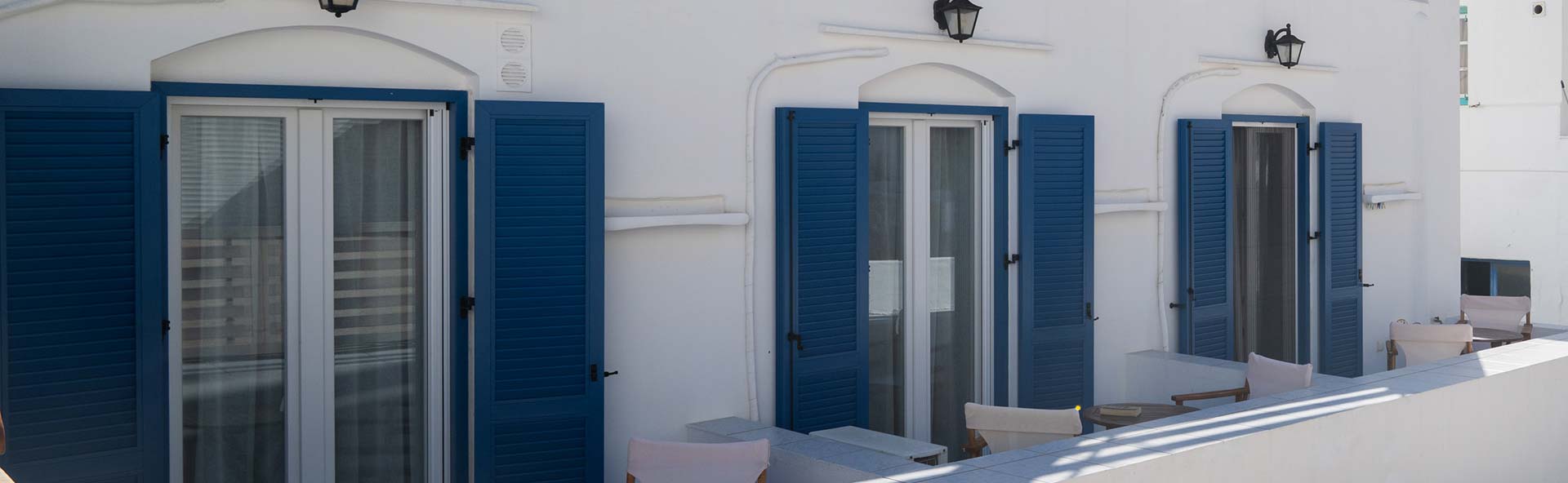 Εξωτερική όψη των δωματίων To Στενό στις Καμάρες Σίφνου με μπλε παντζούρια και καθιστικό έξω